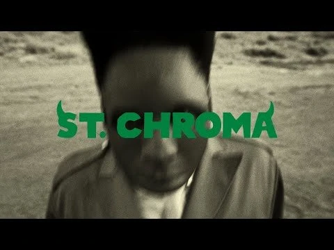 Monochromatic video still shows a person looking down, stylized with green text overlay 'St. Chroma,' set against an outdoor backdrop.