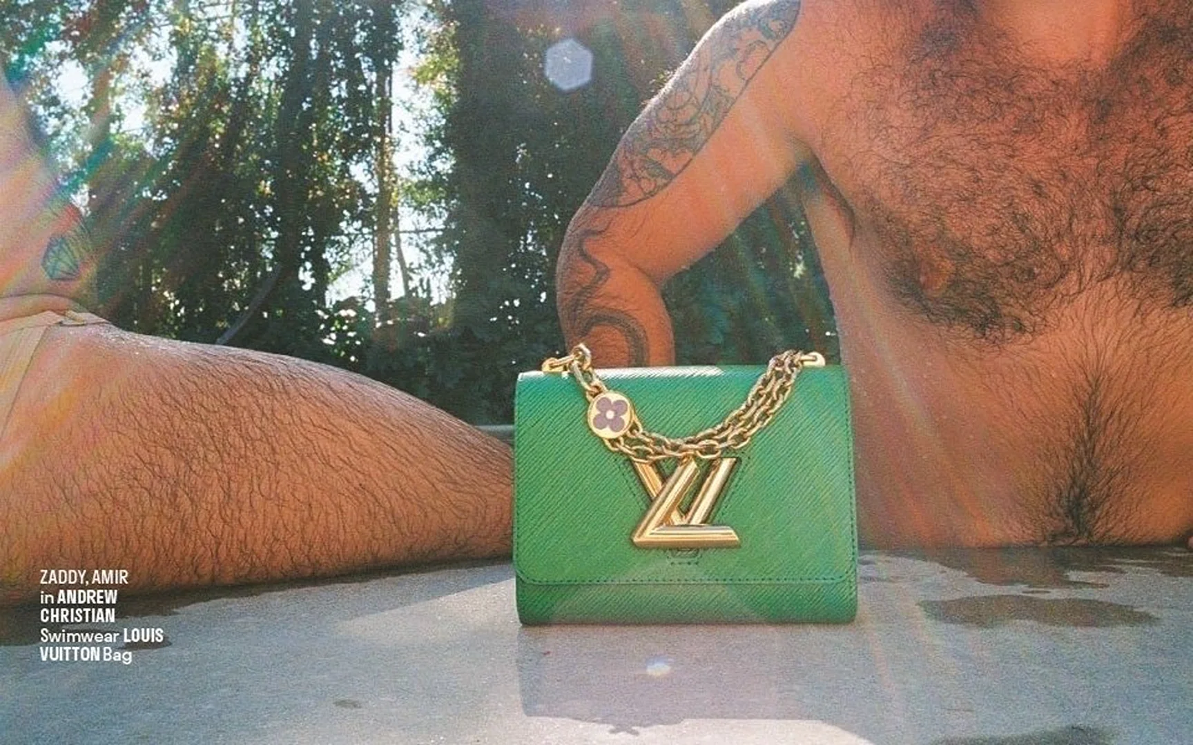 Man in swimwear next to a Louis Vuitton bag. The luxury designer bag is green with a gold chain and logo, and the setting is outdoors.