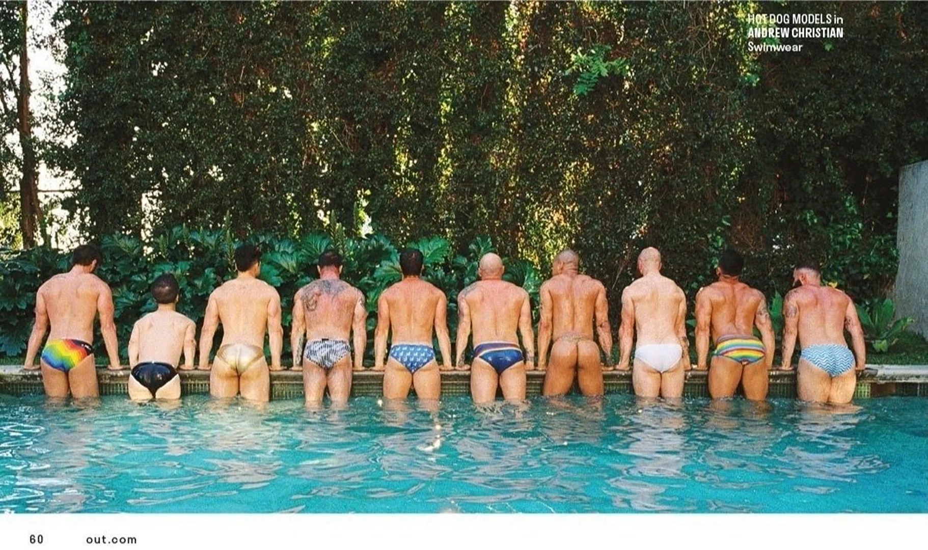 Group of shirtless men in swimsuits standing in a turquoise swimming pool, posing with their backs to the camera against a green leafy background.