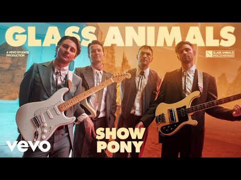 Four musicians stand with guitars and bass guitars in an indoor music video setting, against a stylized backdrop, promoting Glass Animals and their song.