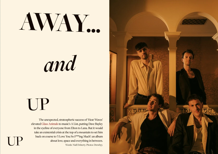 Group portrait of four adult males indoors wearing casual attire in front of a patterned wall with archways and indoor lighting.
