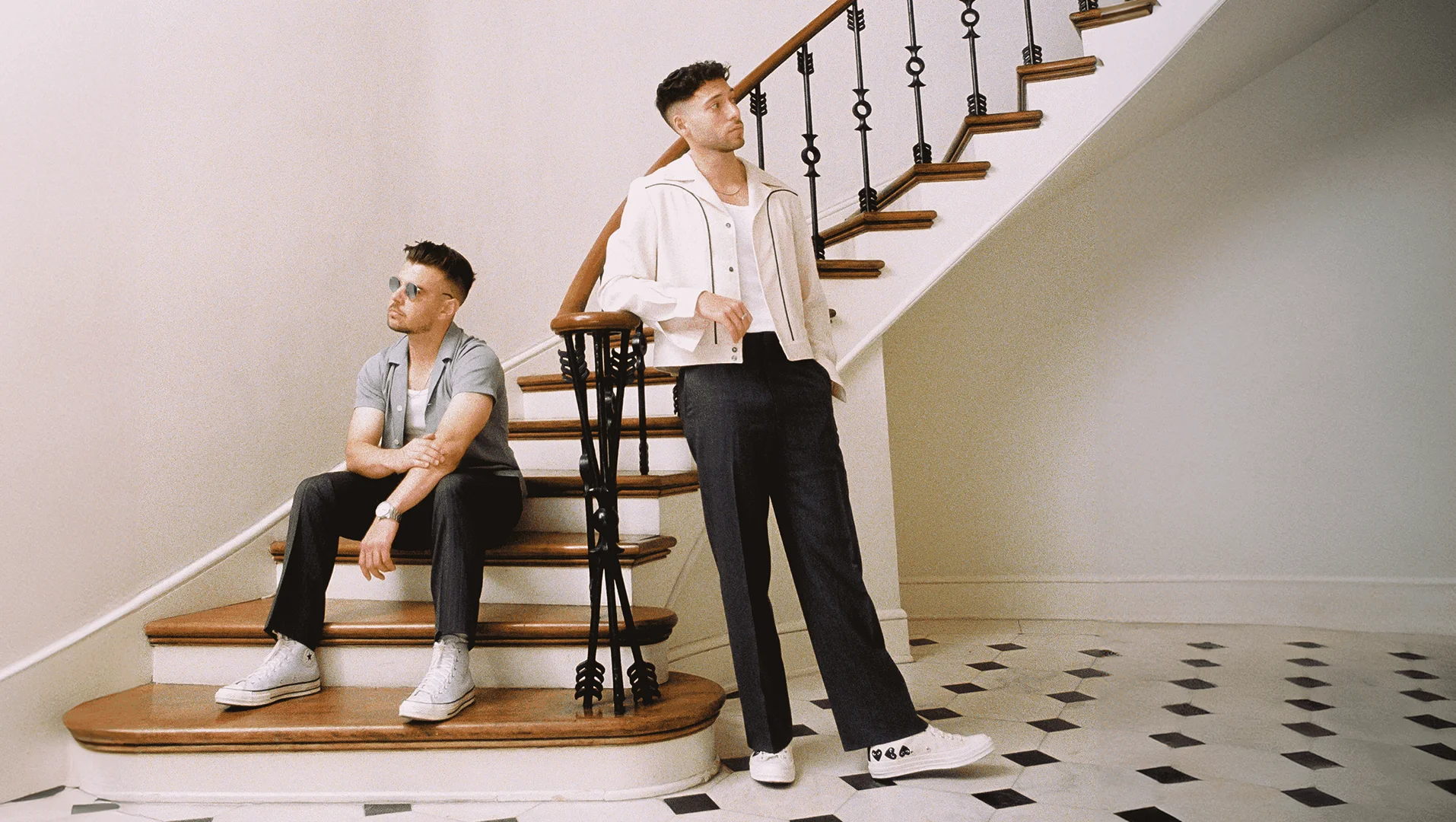 Two men posing on a staircase with a white balustrade and black and white patterned tile floor styled by Kenn Law