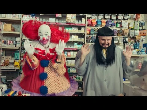 Scene in a convenience store featuring a clown with red hair and white face paint and a man with a bowl haircut and a grey jacket.
