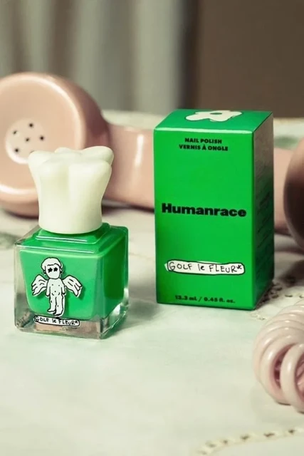 Still life of green Humanrace nail polish bottle and box next to a vintage-style pink telephone on a patterned surface.