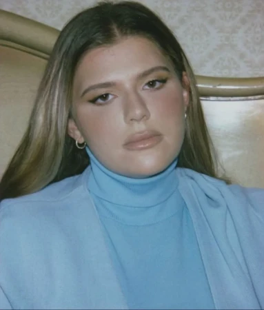 Portrait of a woman wearing a light blue turtleneck and jacket against an upholstered headboard background, styled by Kenn Law.