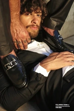 Close-up portrait of a man with curly hair and mustache wearing a black tuxedo, styled by Kenn Law.
