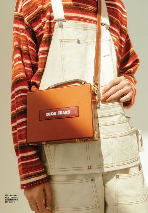 Fashion shot of a person holding a leather handbag with white overalls and a striped shirt, styled with natural lighting.