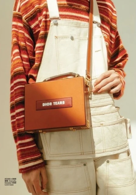 Fashion shot of a person holding a leather handbag with white overalls and a striped shirt, styled with natural lighting.