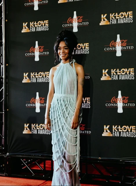 A smiling African-American woman on the red carpet at the K-LOVE Fan Awards, wearing a light blue halter gown with a tiered, rope-like design.