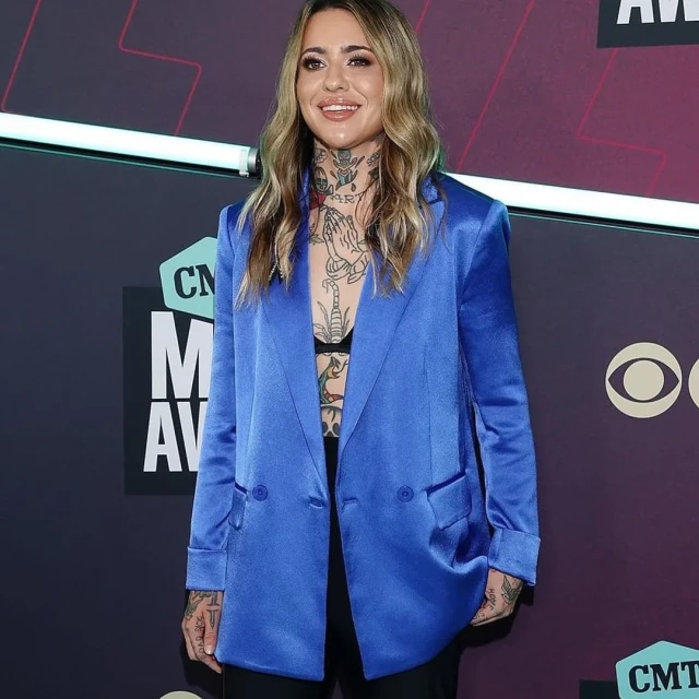 Adult female with tattoos wearing a blue blazer on the red carpet. Celebrity poses for the camera at an entertainment award event.