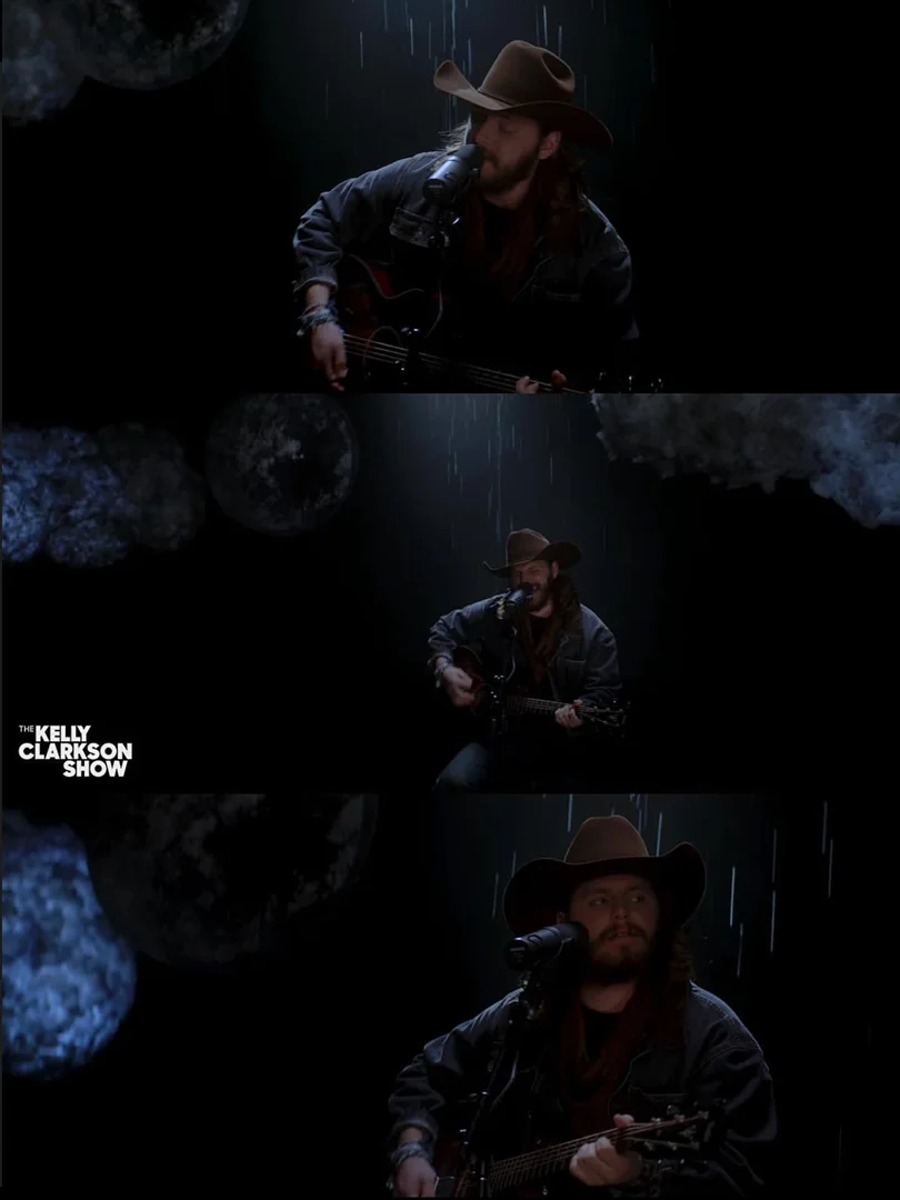 Adult male country singer performing on TV show with cowboy hat, acoustic guitar, microphone in a dark studio with a simulated rain effect.