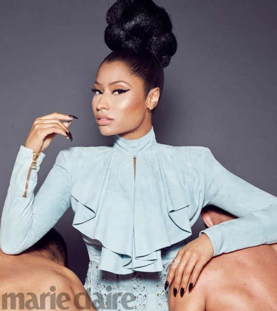 Nicki Minaj poses in a light blue outfit with a high bun hairstyle, leaning on two male figures in a studio setting for Marie Claire.