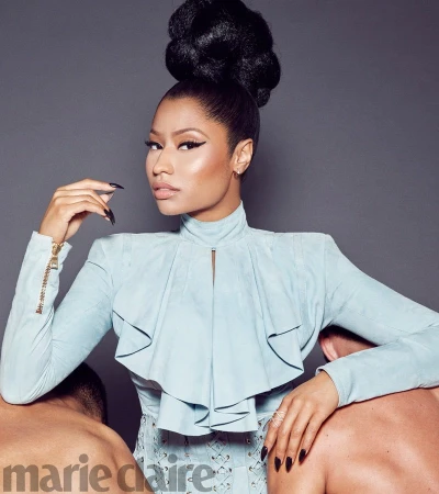 Nicki Minaj poses in a light blue outfit with a high bun hairstyle, leaning on two male figures in a studio setting for Marie Claire.