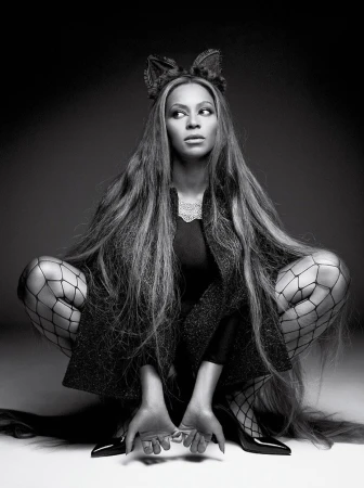 Black and white portrait of a woman with long hair, fishnet stockings, cat ears, and high heels crouching against a dark background.