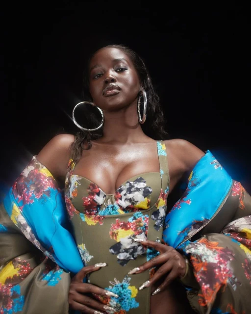 Portrait of an African American woman wearing a floral bodysuit and a floral puffer jacket over her shoulders in front of a black background.