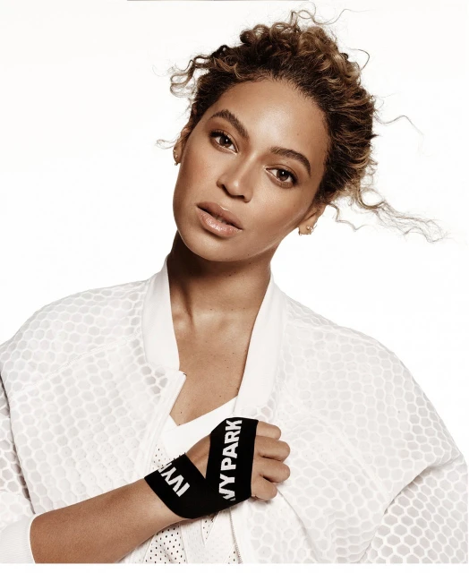 Beyoncé poses in a white sports jacket with 'Ivy Park' branded wristbands in a studio, showcasing fashion and fitness.