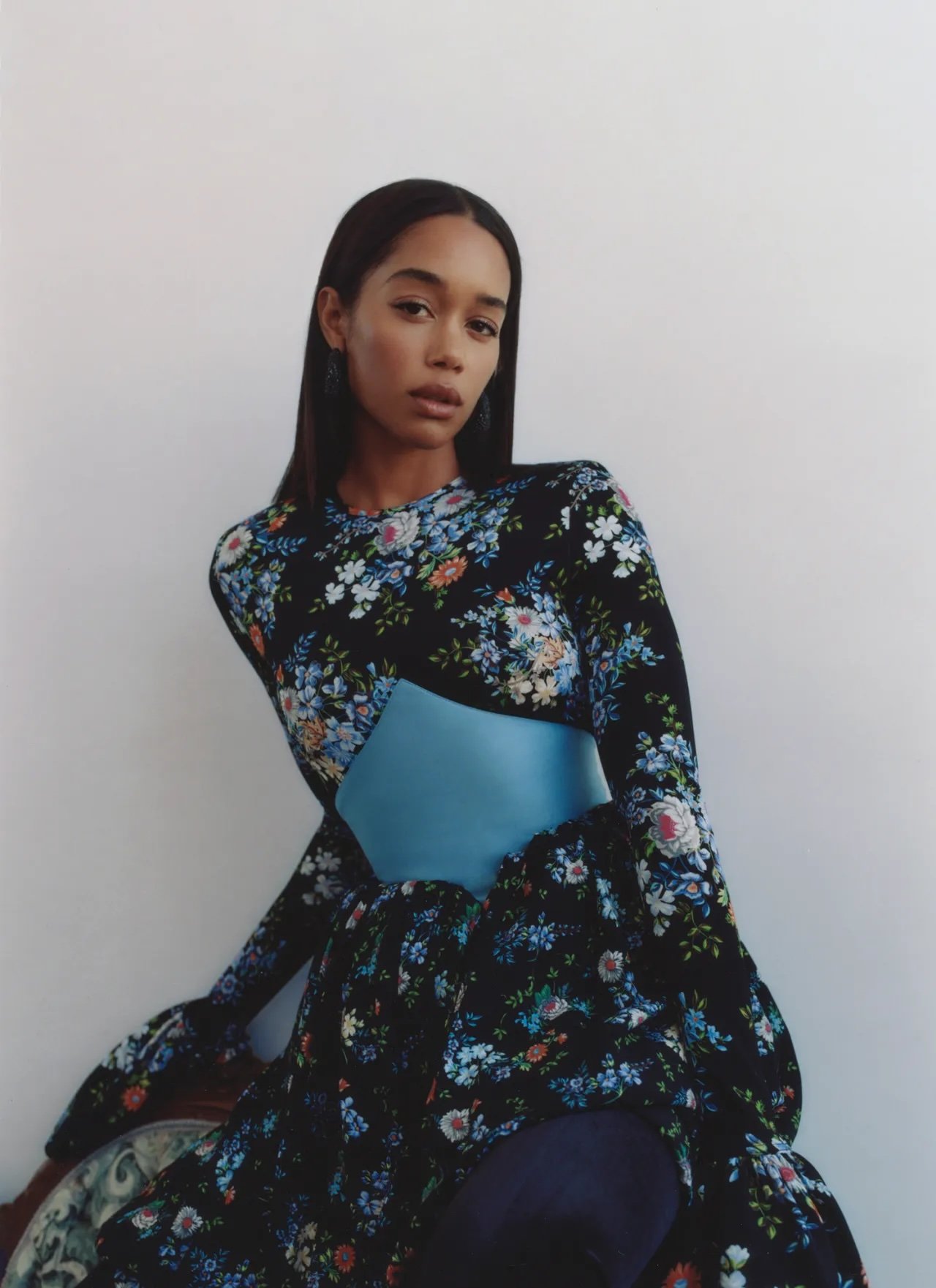 Woman with long dark hair wearing a black floral long-sleeve dress with a blue satin cummerbund.