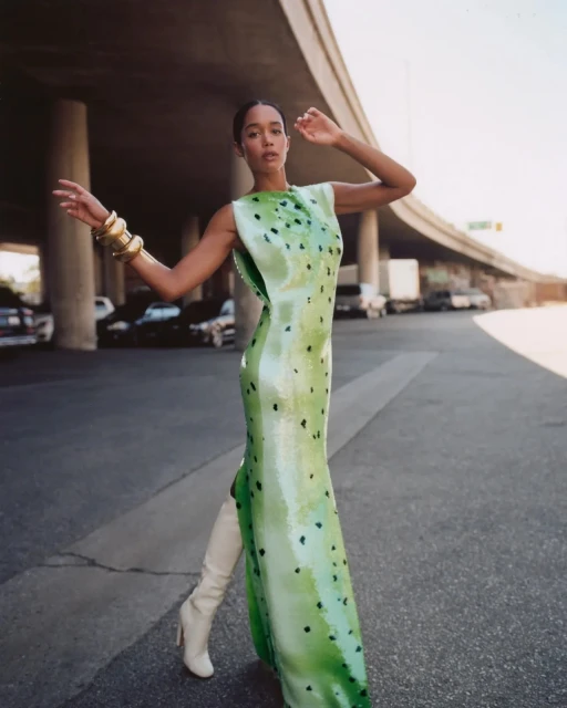 Adult female fashion model poses in a green spotted evening gown with beige thigh high boots on a city street under a highway overpass.
