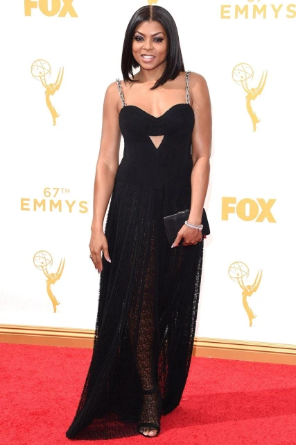 Elegant woman in a black gown on a red carpet at an awards ceremony, captured in a full shot with a backdrop of event branding.