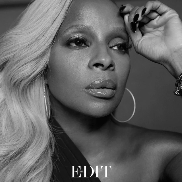 Close-up black and white portrait of a woman with blonde hair, hoop earrings, and a hand near her face. Glamour shot.