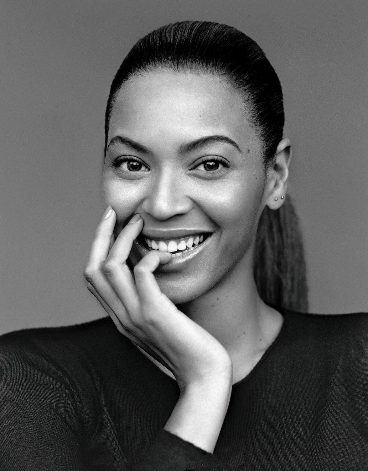 Black and white portrait of a smiling woman with her fingers touching her face, set against a neutral background in a close up shot.