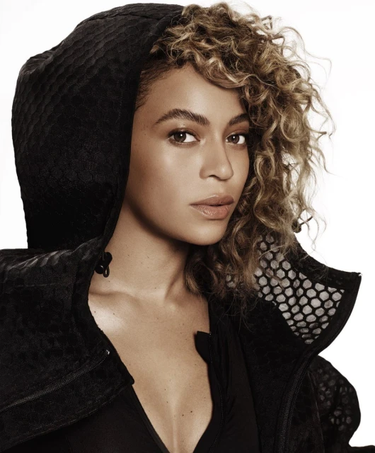 Close-up portrait of a woman with curly hair wearing a hooded jacket, set against a white background. Beauty and fashion aesthetic.