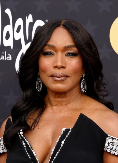 Close-up portrait of Angela Bassett in a black dress, smiling on a red carpet with decorative earrings and black wavy hair.