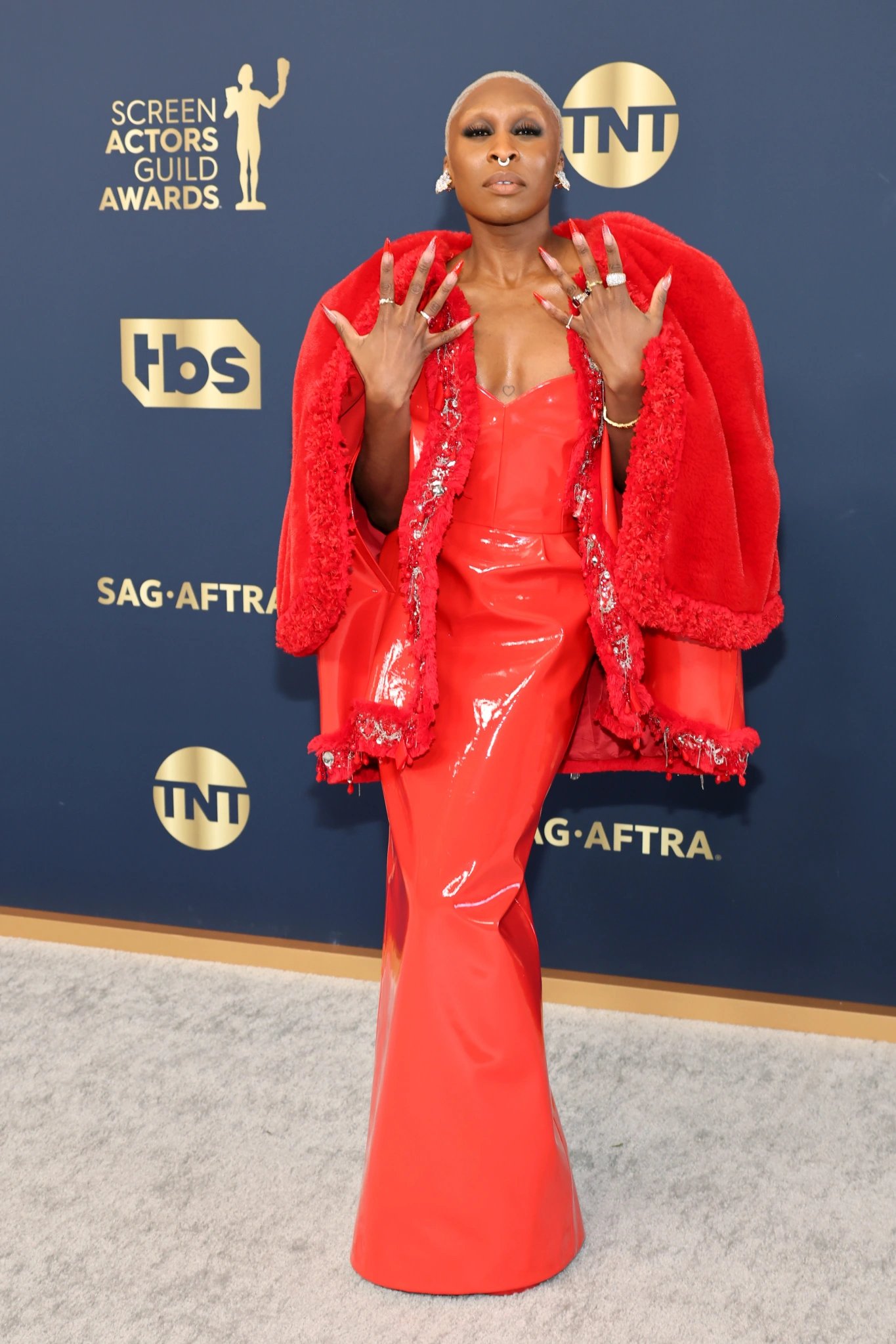 Cynthia Erivo poses in a red gown and faux fur coat on the red carpet at the Screen Actors Guild Awards. 