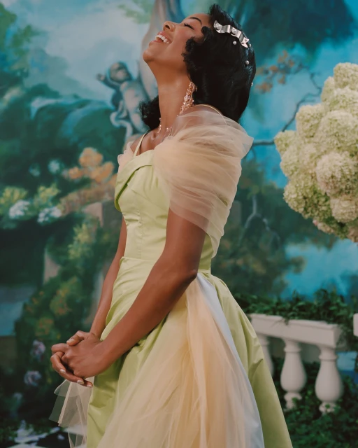 Elegant woman in a green and cream gown smiles with her head tilted back in a lighthearted moment, set against a painted backdrop.