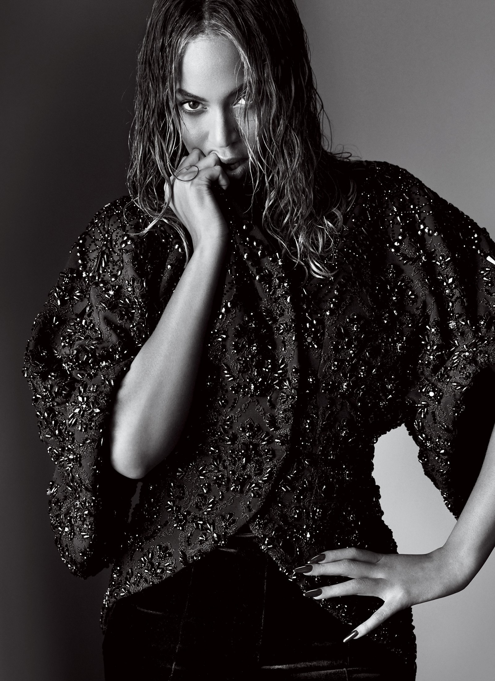 Black and white portrait of a glamorous woman with wet hair, wearing a beaded top with hand near her face and hand on her hip.
