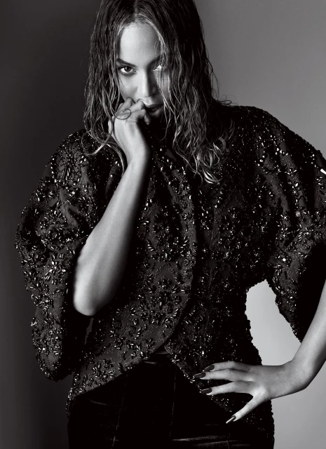 Black and white portrait of a glamorous woman with wet hair, wearing a beaded top with hand near her face and hand on her hip.