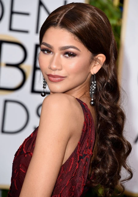 Zendaya poses in a close-up shot at an event, showcasing her dark brown hair, elegant earrings, and a dark red patterned dress.
