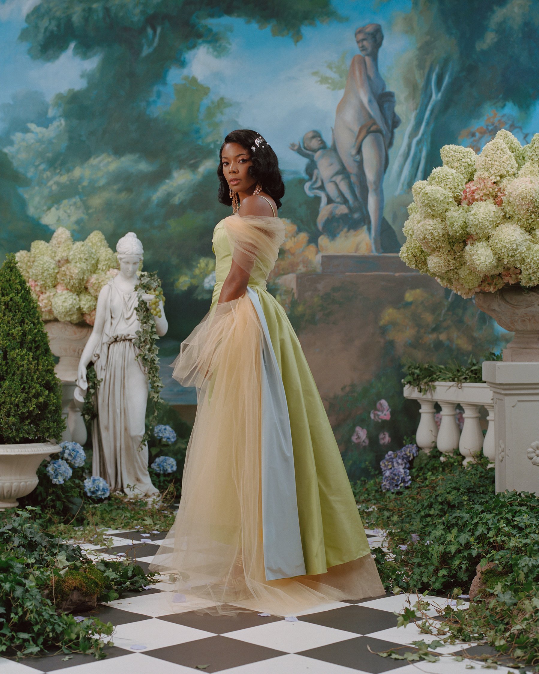Elegant woman in a green gown poses in a garden setting with statues, a checkered floor, and lush foliage in a painterly style.