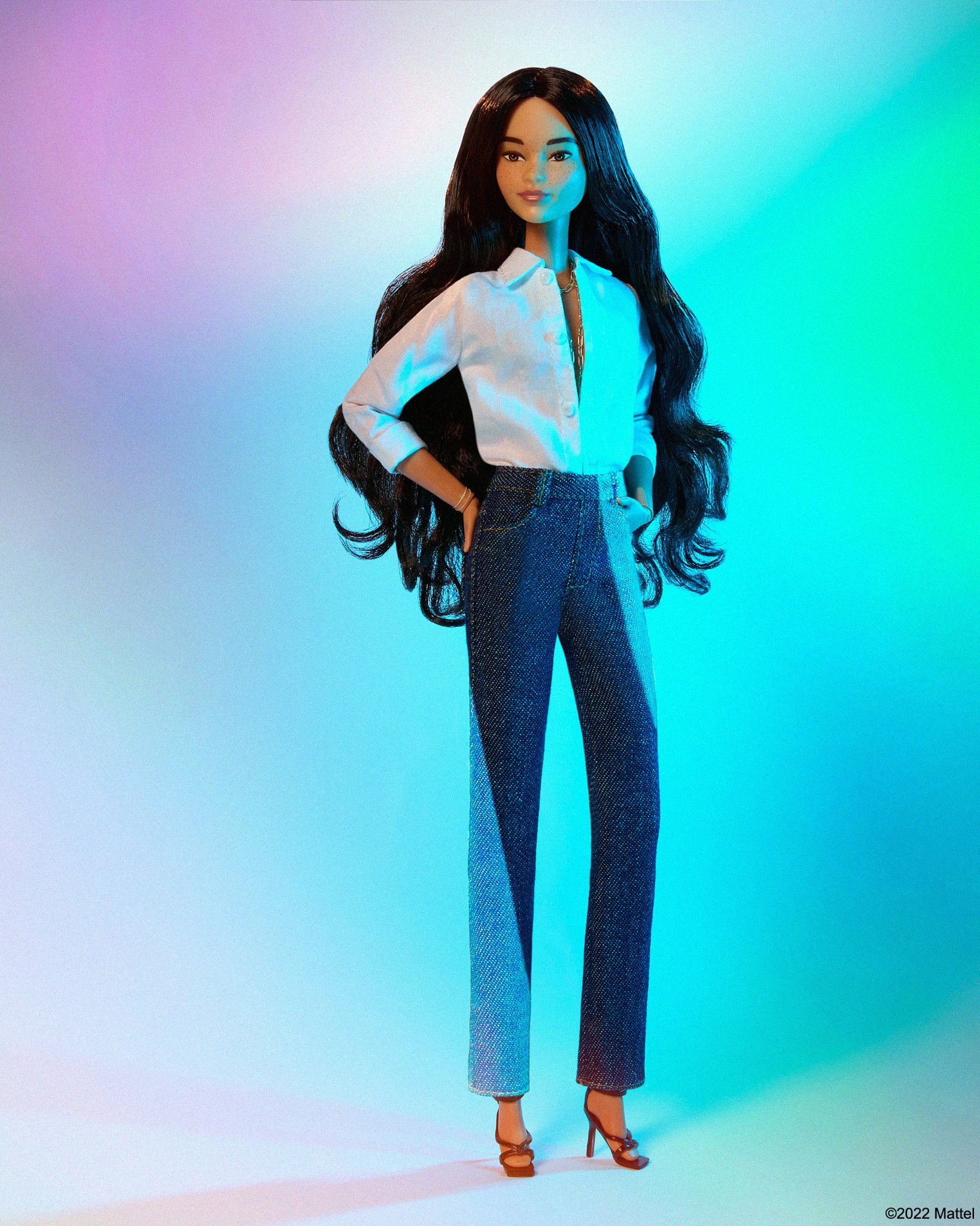 Fashion doll with long, dark hair wears a white collared shirt, two-tone jeans, and brown heels against a softly lit gradient background.