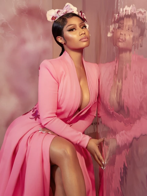 Portrait of a woman in a pink dress with floral headpiece, posing against a pink backdrop with a reflective surface showing her reflection.