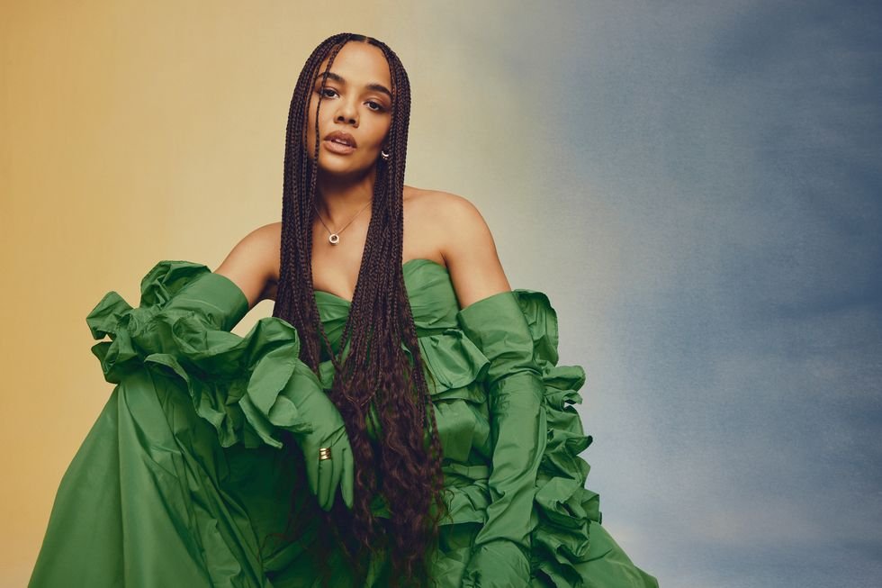 Portrait of a Black woman in an emerald green gown with an off-the-shoulder neckline against a mixed yellow and blue background.