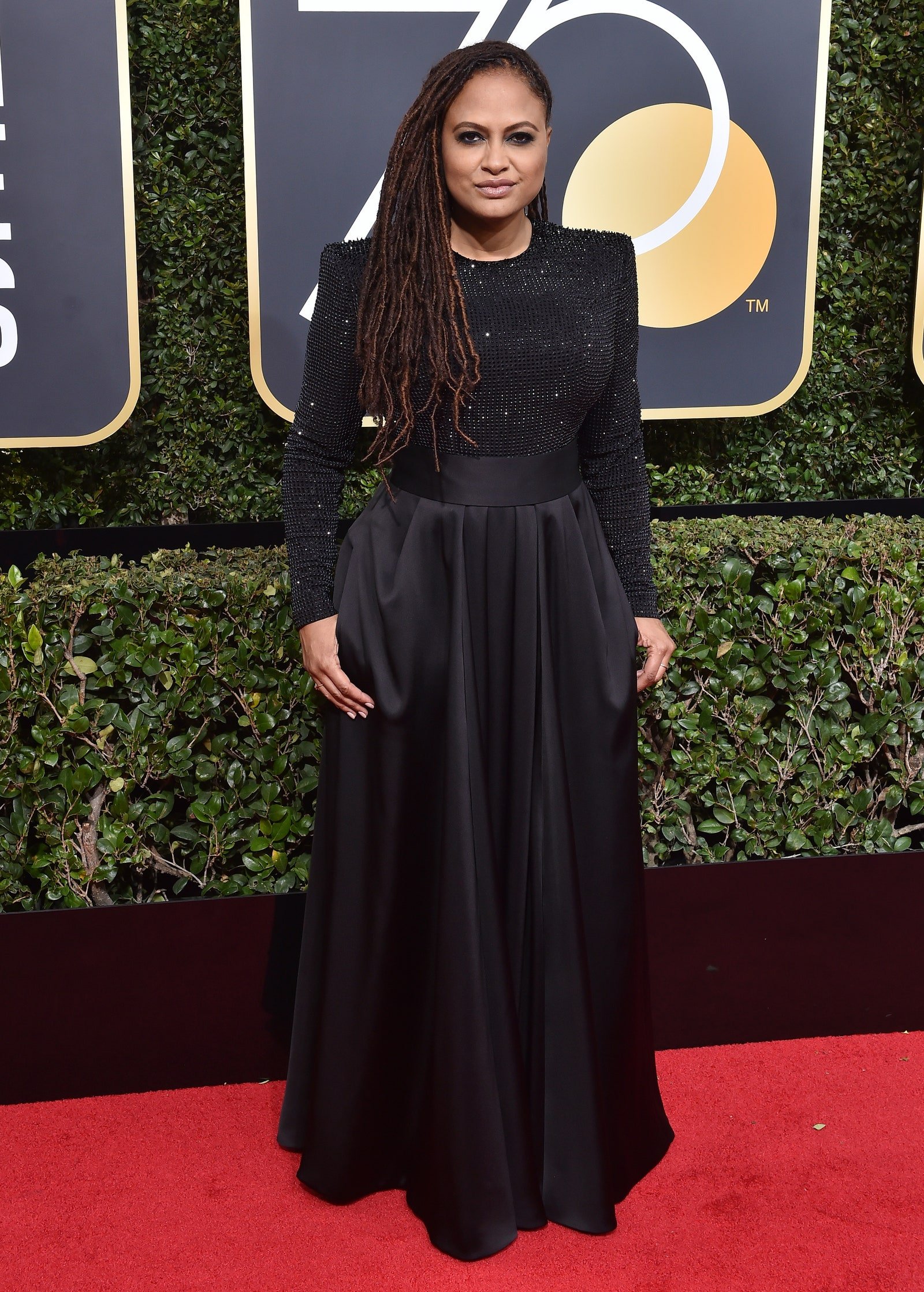 Ava DuVernay poses in a long-sleeved black gown with an embellished top and a full skirt on a red carpet at an awards show.