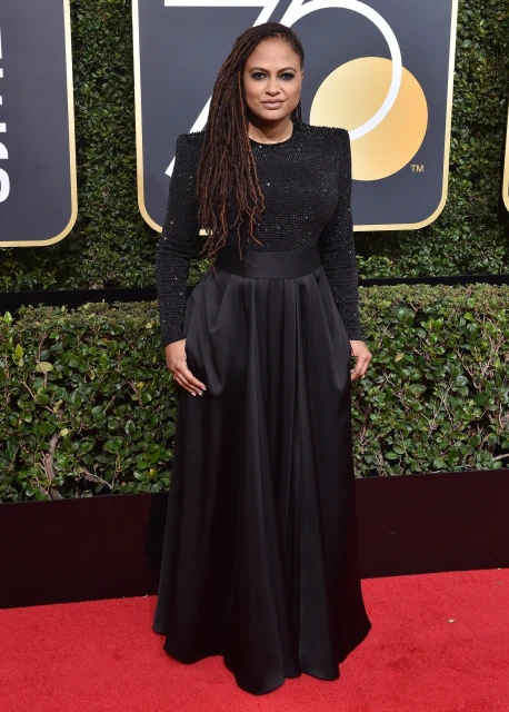 Ava DuVernay poses in a long-sleeved black gown with an embellished top and a full skirt on a red carpet at an awards show.