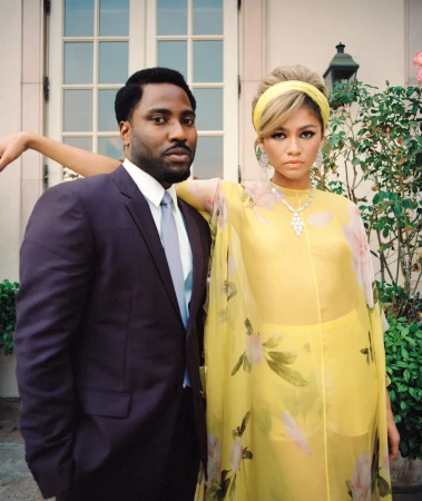 Portrait of an African-American man in a suit and a blonde woman in a yellow floral dress standing in front of a building.