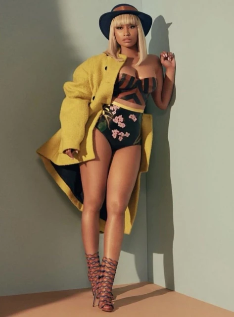 Woman in patterned swimsuit and yellow coat posing against a wall, wearing hat and strappy heels in a fashion portrait.