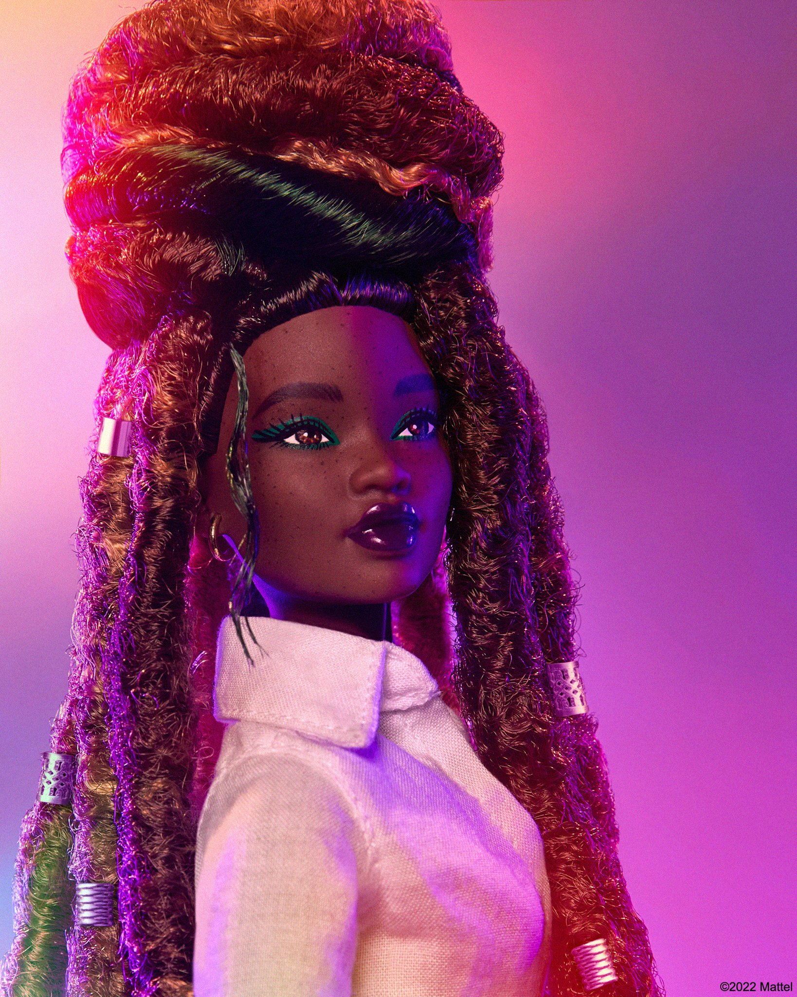 Fashion doll with dark skin, styled locs, wearing a light pink top, showcased against a vibrant purple and pink gradient background.