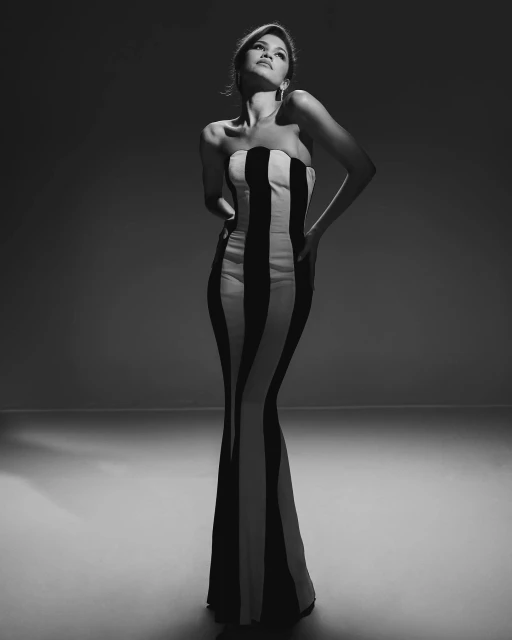 A full shot captures a woman in a striking strapless black and white gown, set against a dark backdrop in a photo studio.