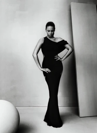 A woman in a black, one-shoulder dress poses in front of a studio backdrop. The black and white image captures her elegance and style.