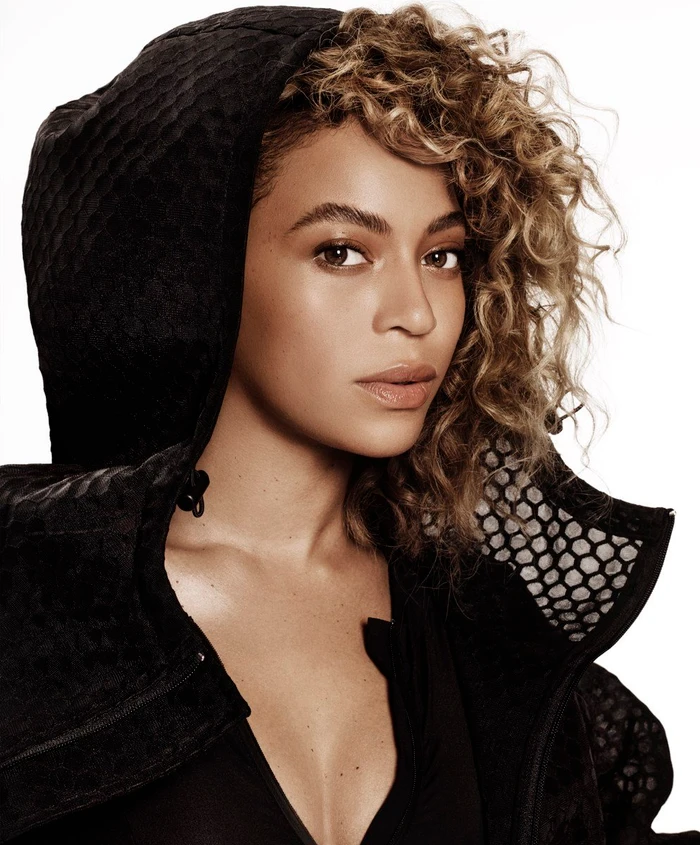 Portrait of Beyonce wearing a black hooded jacket with textured mesh details against a plain white background