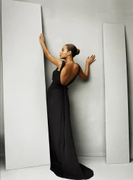 Woman in a long black evening gown posing between tall panels with her hair styled in a neat bun, captured by Kim Kimble.
