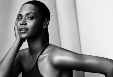 Monochrome portrait of a woman with slicked-back hair resting her hand on her cheek against a light backdrop