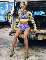 Beyonce sitting on the back of a truck wearing a yellow floral crop top and purple patterned briefs with stockings and cat-eye sunglasses.