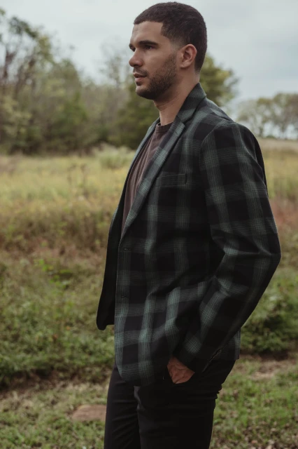 Man in plaid blazer in grassy field.  Portrait shot of stylish adult male in nature setting, looking left with neutral expression.
