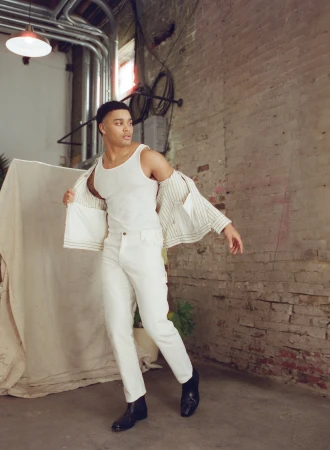 Black man wearing a white tank top and white trousers with a striped jacket styled by Kinsey Ranee