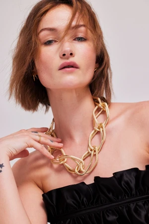 Model wearing a chunky gold chain necklace and a black strapless top against a white background